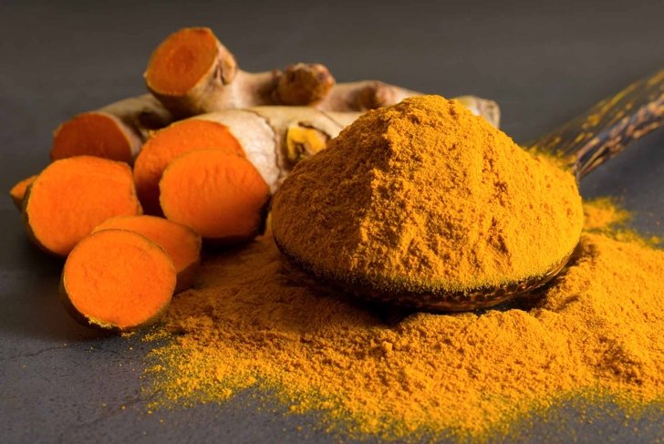 Turmeric (curcumin) powder in a wooden ladle and fresh rhizome on a black background,For spices and medicine.