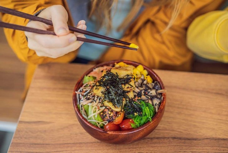 Woman eating Raw Organic Poke Bowl with Rice and Veggies close-up on the table. Top view from above horizontal