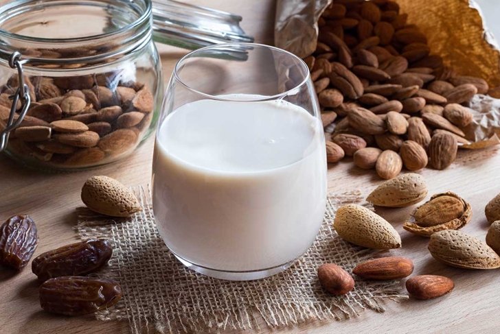 A glass of almond milk on a wooden table with almonds and dates