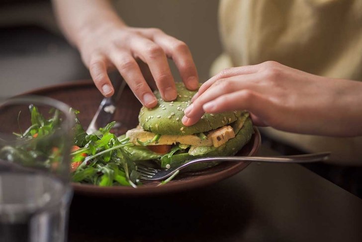 Picture of vegan dish represented on wooden plate. Lady\'s hands taking vegan burger from plate in vegan restaurant or cafe.