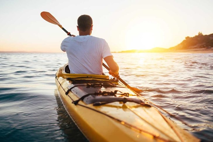 Rear view of kayaker man paddle kayak at sunset sea. Kayaking, canoeing, paddling