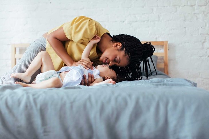 Beautiful African woman cuddling her baby daughter in bedroom.
