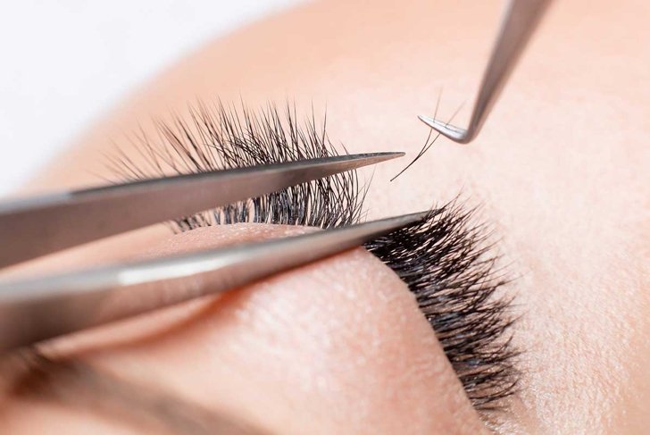 Eyelash extension procedure. Master tweezers sets fake lashes on beautiful woman.