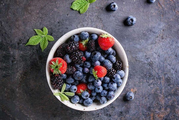 Spotted ceramic bowl with assortment berries blueberries, strawberries and blackberries at old black board over wooden table. Rustic style. Top view