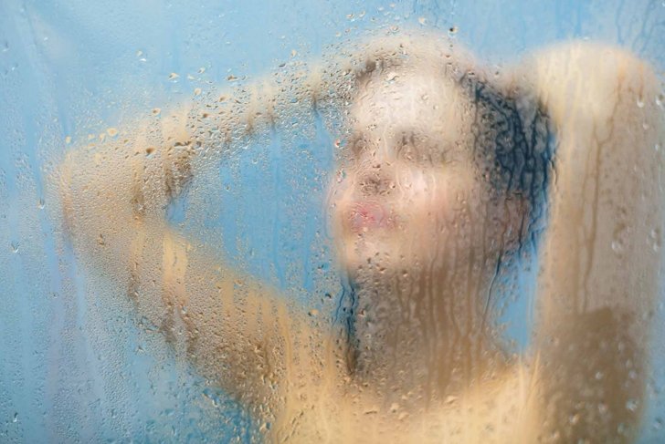 Taking moment for yourself. Relaxed unrecognizable woman stands in shower cabin under hot water, feels relief after stressful day, takes care of her body and skin. Relaxation and hygiene concept