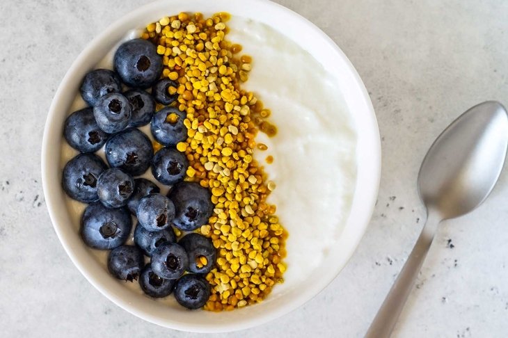 Bowl of greek yogurt, bee pollen and fresh berries on white stone background. Healthy breakfast. Top view.