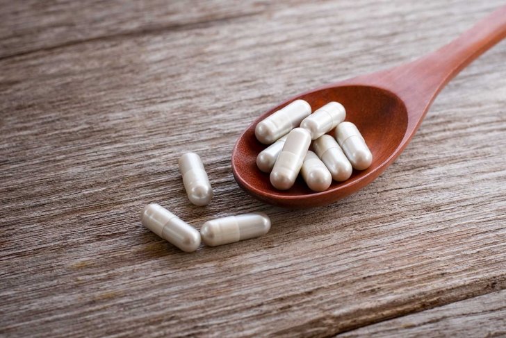 White gingsen herbal medicine capsules pill in wooden spoon isolated on wood table background.