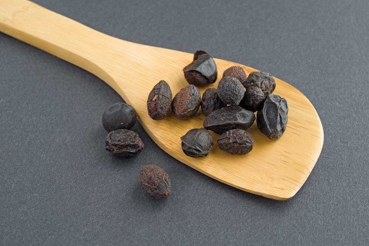 A wood spoon with saw palmetto berries on a dark background.