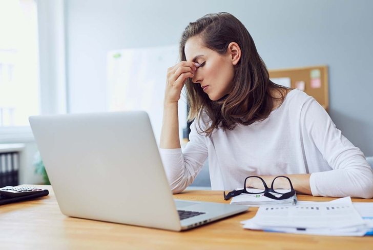 Beautiful stressed young office worker sitting at desk holding head because of pain in office