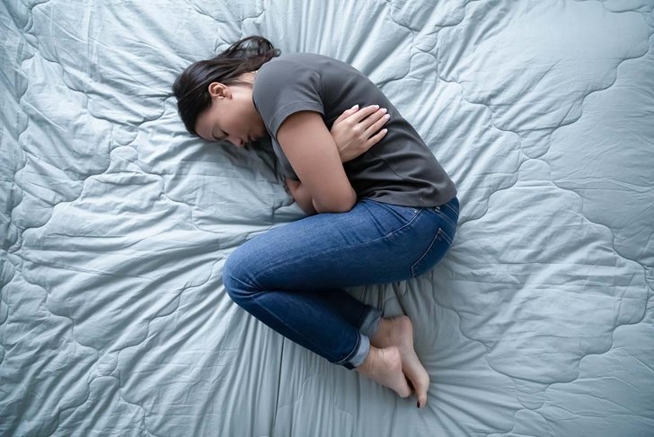 Top view of unhappy depressed young woman lying on bed suffer from abortion or miscarriage, upset female hunch crook in bedroom sleep having emotional breakdown or crisis, healthcare concept