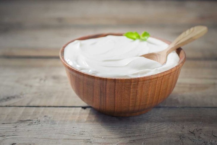 Greek yogurt in a wooden bowl on a rustic wooden table. Selective focus