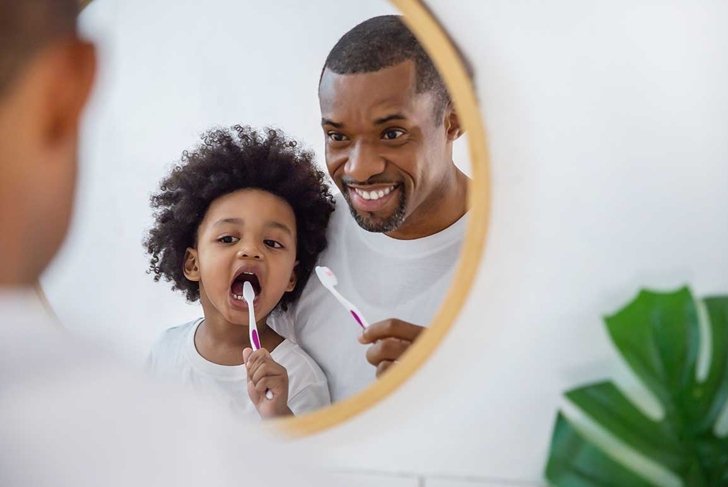 Portrait of happy family black African American father and son child boy brushing teeth in the bathroom. Morning routine with toothbrushes, fatherâ€™s day concept