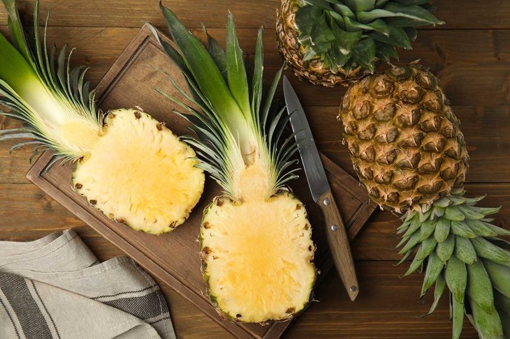 Whole and cut pineapples on wooden table, flat lay