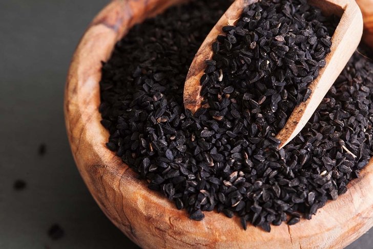 Black cumin or nigella sativa or kalonji seeds in bowl with spoon on black slate background, selective focus