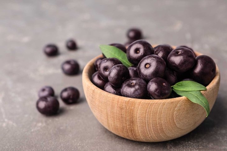 Bowl of fresh acai berries on grey stone table, closeup view. Space for text