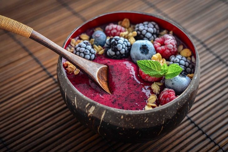 Acai smoothie bowl with blueberry, blackberry, raspberry, granola and chia seeds in bowl from coconut shell