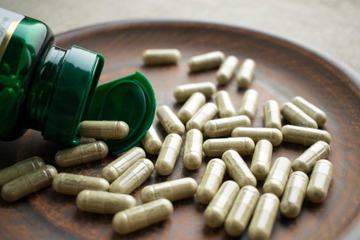 Close up Green capsules ginkgo biloba, bottle on clay brown plate on a burlap background. Dietary supplements for healthy brain, memory. Vitamins and minerals for vegans and vegetarians. Superfood