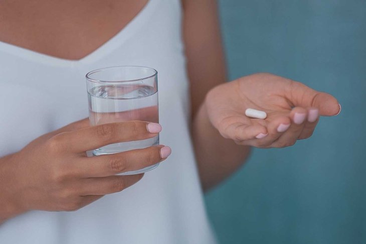 Woman arm holding small round med and glass of water before taking medication, shallow depth of field, focus on medicine