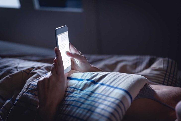 Woman using phone late at night in bed. Person looking at text messages with cell in dark home. Hipster online dating or texting with smartphone. Sexting or cheating concept. Smart device screen light