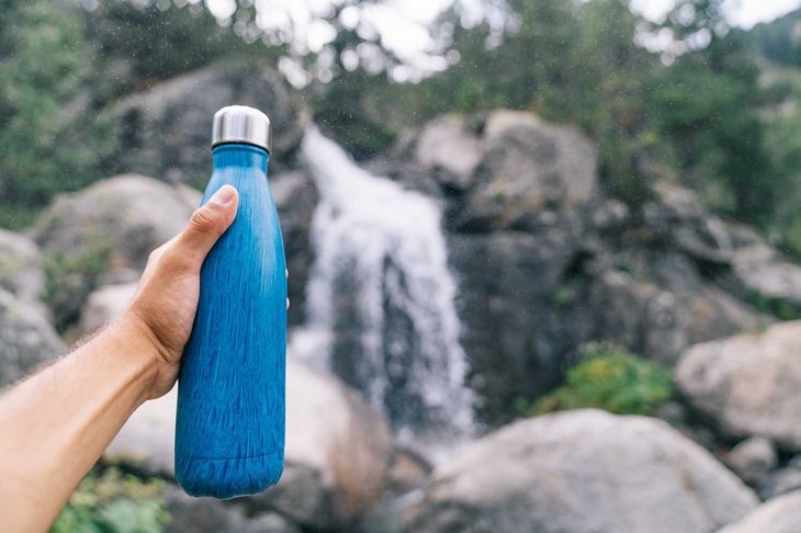 Sustainable and reusable water bottle. Hand holding a blue Eco Friendly Water Bottle. Goodbye to single use plastic bottles. Plastic free and zero waste. Sustainable life.