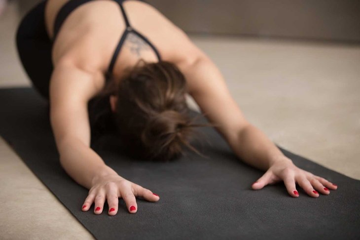 Young attractive woman practicing yoga, stretching in Child exercise, Balasana pose, working out, wearing black sportswear, urban style grey studio floor, close up, focus on fingers