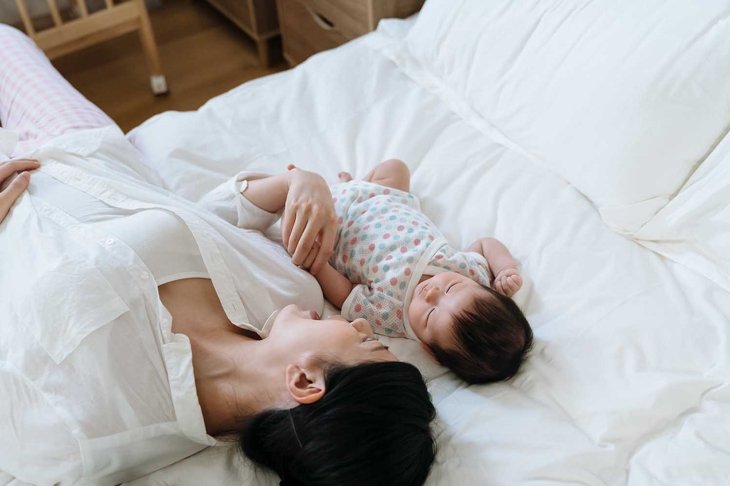 high angle view korean mother lying on bed with her young child. asian woman face to her baby daughter just put her kid to bed by singing gently to her.