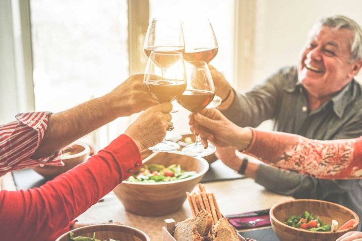 Senior friends cheering with wine glasses at home lunch - Happy mature people having fun together - Focus on left bottom glass - Joyful elderly lifestyle concept