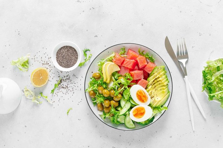Ketogenic, keto or paleo diet lunch bowl with salted salmon fish, lemon, avocado, olives, boiled egg, cucumber, green lettuce salad and chia seeds. Healthy food trend. Top view