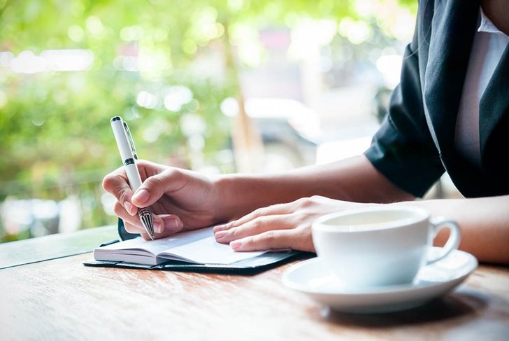 close up of woman writing journal and cup of coffee