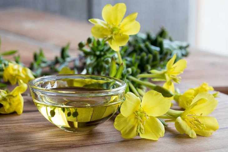 Evening primrose oil in a glass bowl, with fresh evening primrose flowers in the background