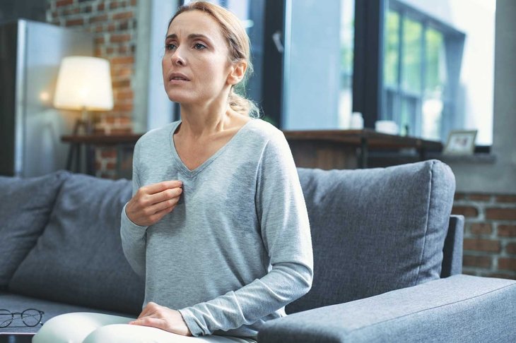 Hot flashes. Exhausted mature woman resting on sofa and having hot flash