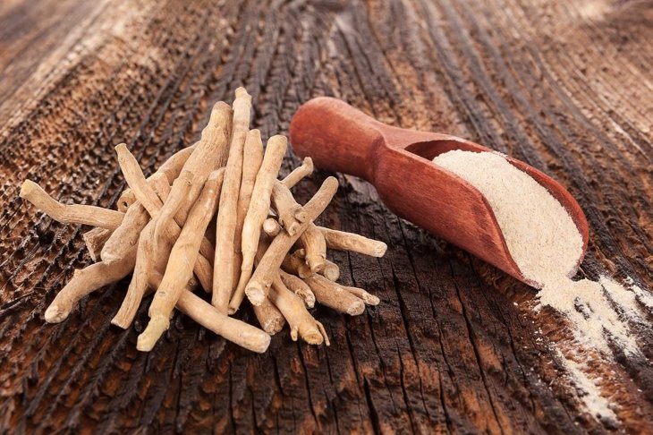 Ashwagandha superfood powder and root in spoon on wooden table.