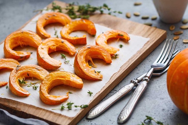 Baked pumpkin slices with thyme on a wooden board over grey table. Seasonal food vegetarian recipe.
