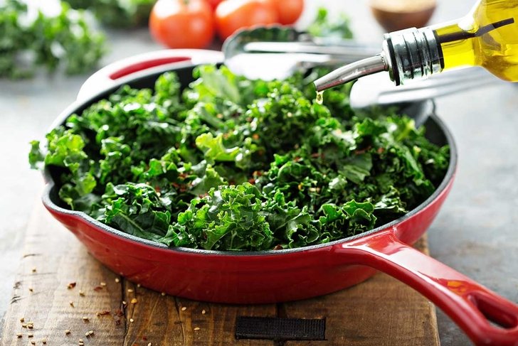 Quickly sauteed kale with chili flakes in a cast iron pan with olive oil pouring over, healthy cooking concept