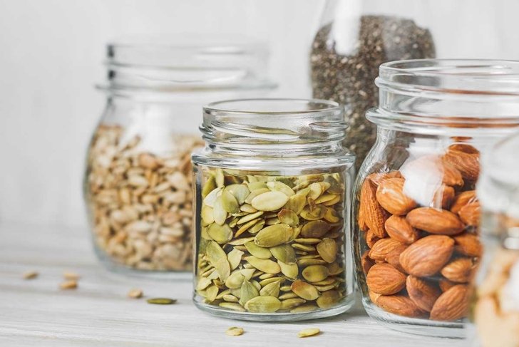 Various nuts and seeds in glass jars over white wooden table against white background. The concept of vegetarian and organic food. Set of photos.