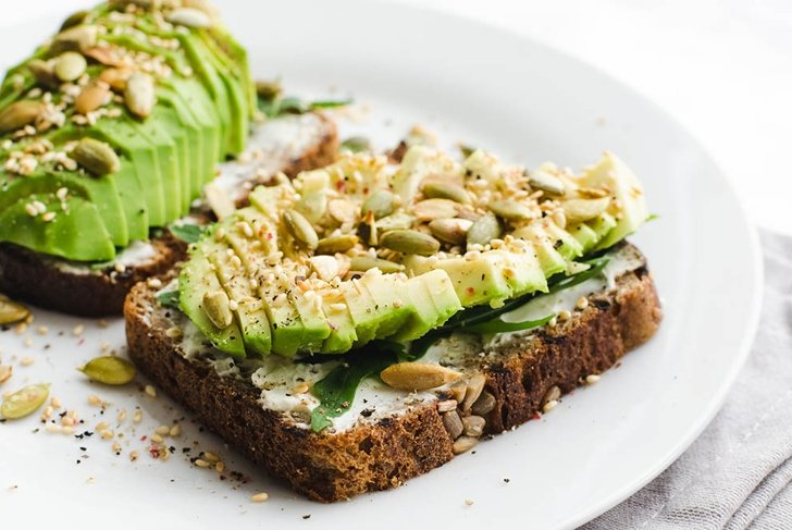 Healthy avocado toasts for breakfast or lunch with rye bread, sliced avocado, arugula, pumpkin and sesame seeds, salt and pepper. Vegetarian sandwiches. Plant-based diet. Whole food concept.